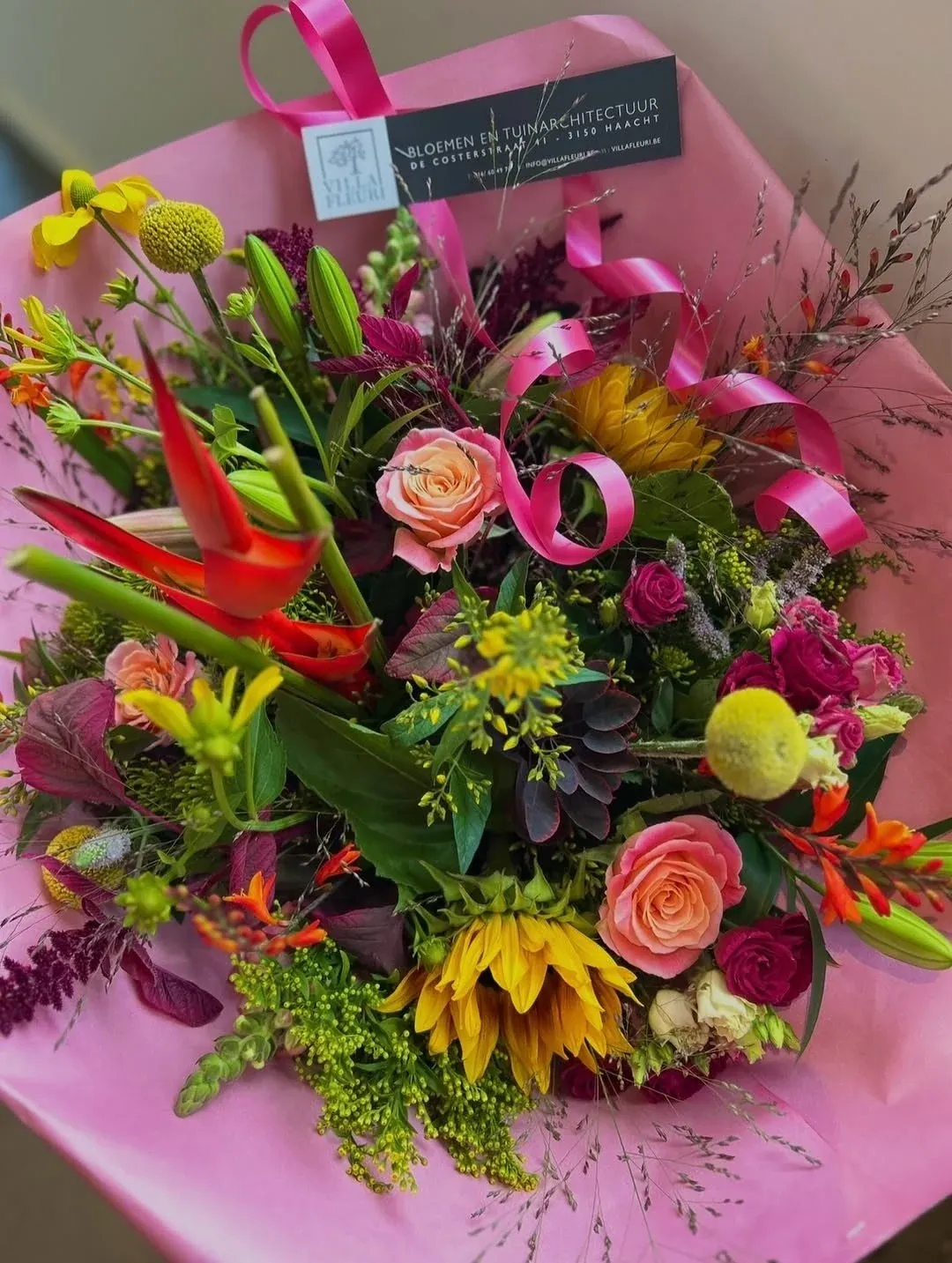 Kleurrijk boeket met heliconia, rozen en zonnebloemen, ingepakt in roze papier met lint