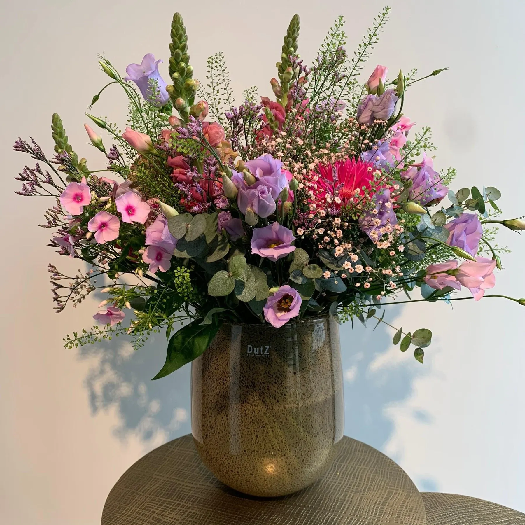 Luchtig pastelboeket met gerbera, lisianthus en eucalyptus in een glazen vaas