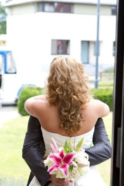 Bruid en bruidegom van achteren, met een boeket van roze lelies