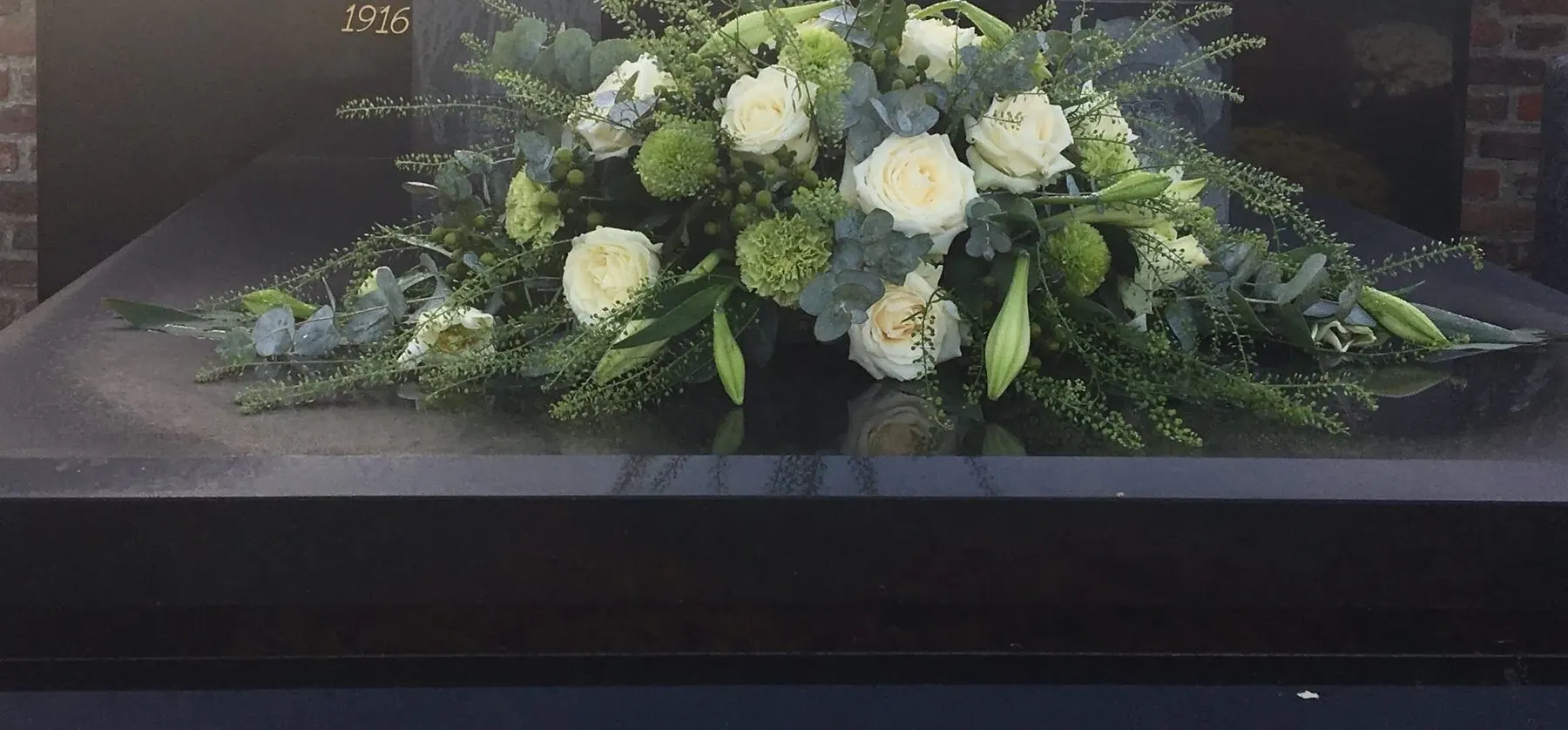 Grafstuk van witte rozen en groen op een grafsteen