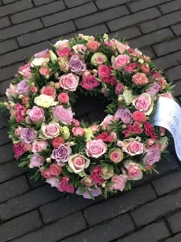 Rouwkrans van pastelroze en lila rozen met een lint