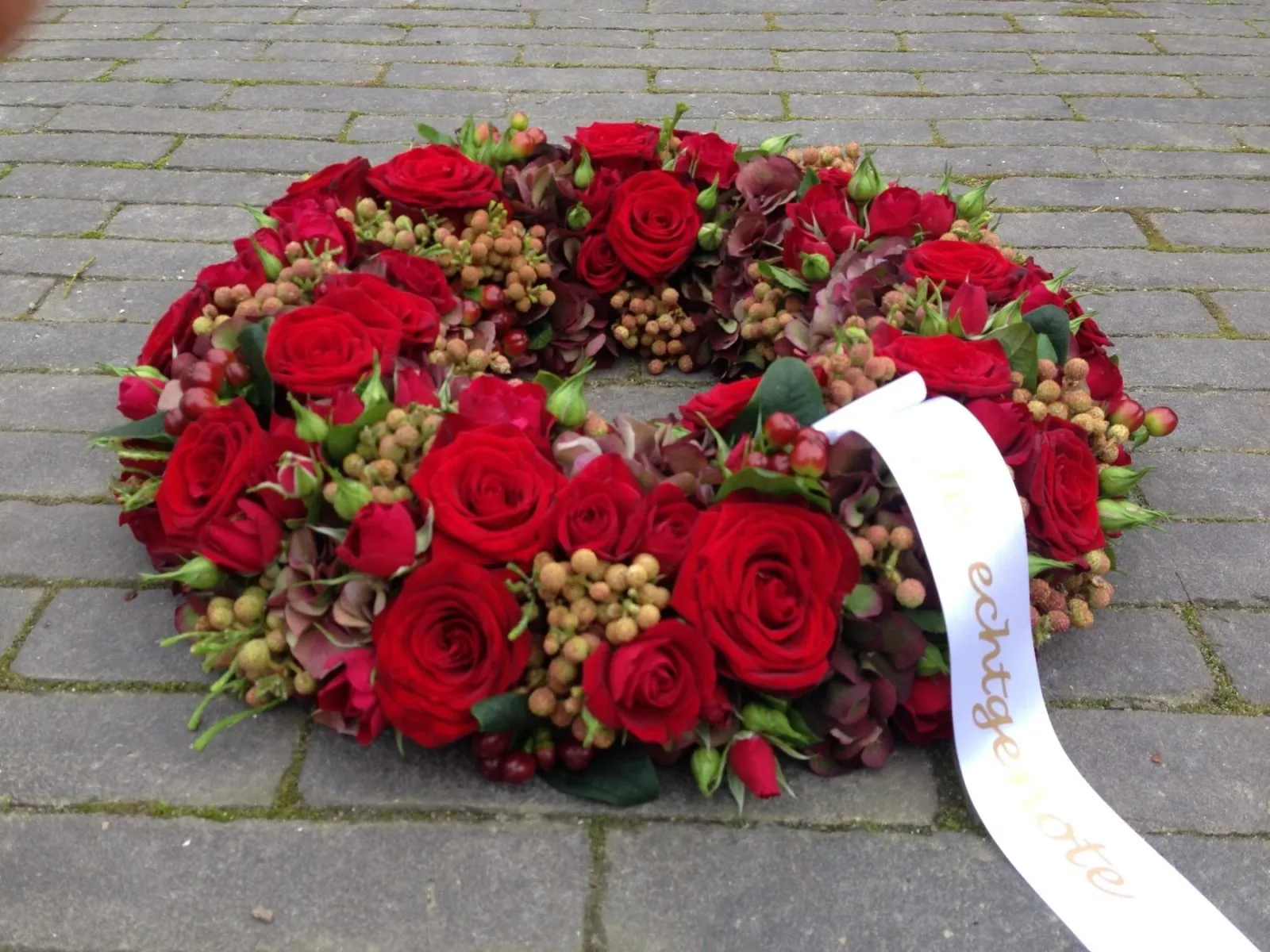 Rouwkrans van rode rozen en bessen met een wit lint