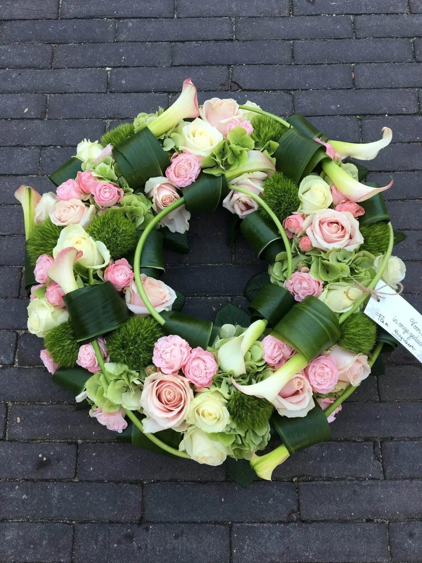 Rouwkrans met roze rozen, witte calla’s en gevlochten blad
