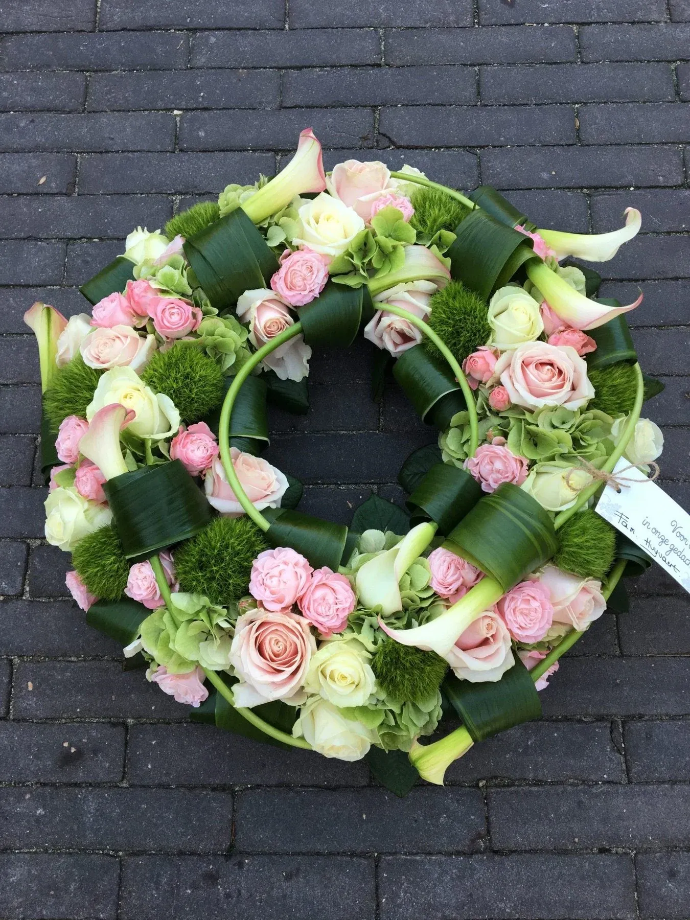 Rouwkrans met roze rozen, witte calla’s en gevlochten blad
