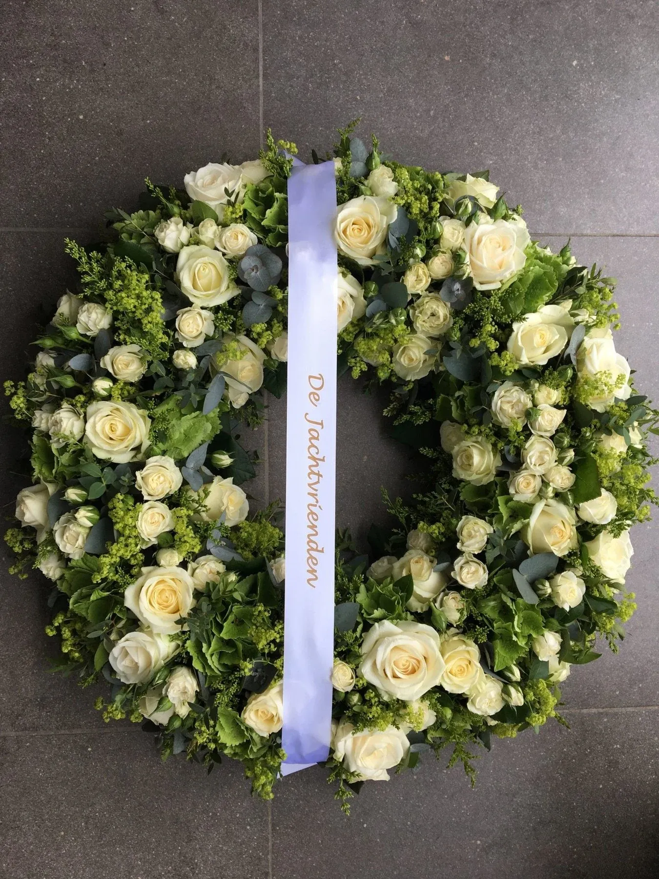 Rouwkrans van witte rozen en groen met een lint