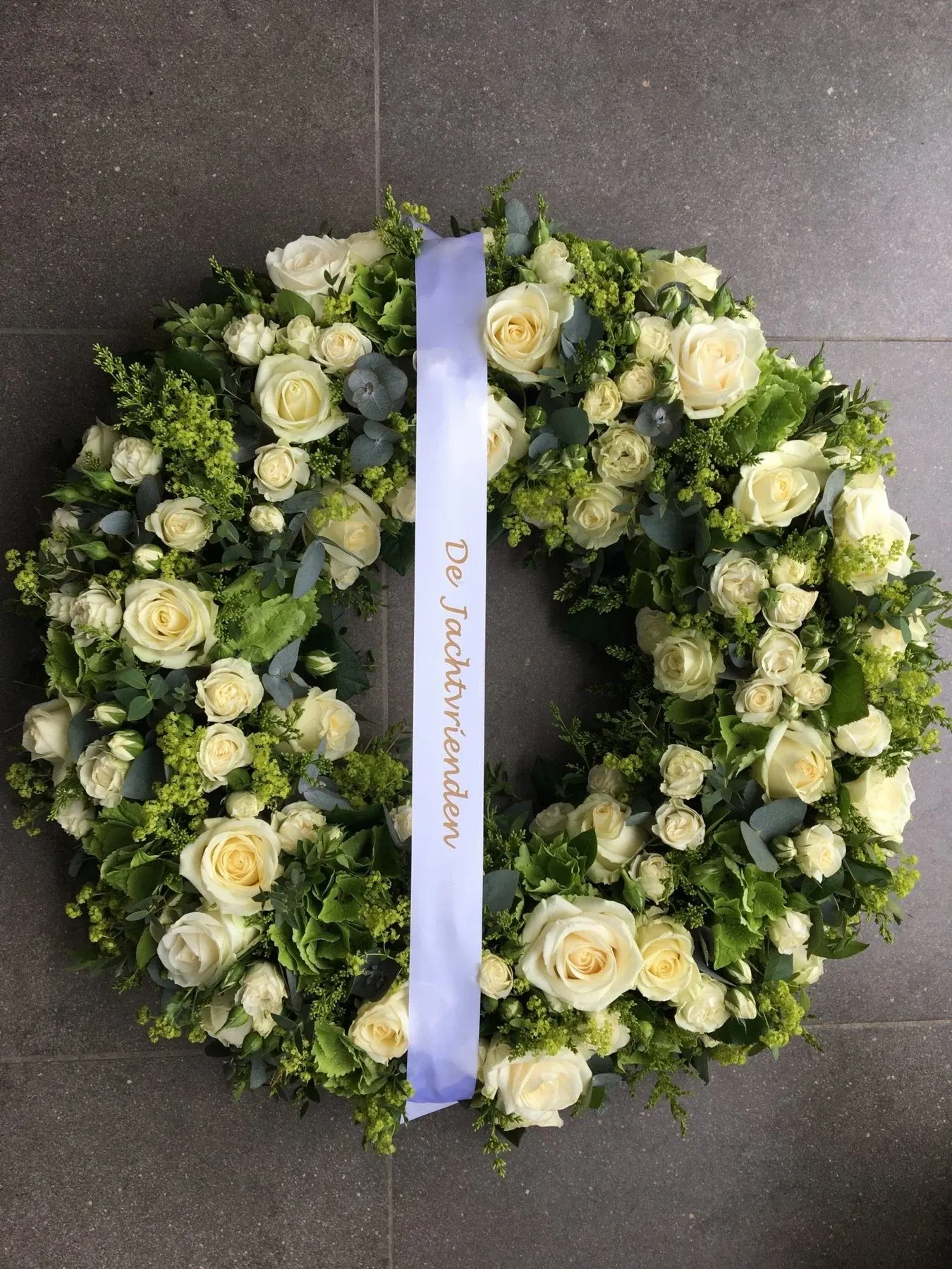 Rouwkrans van witte rozen en groen met een lint