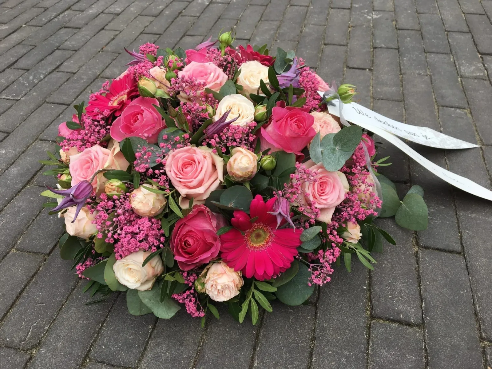 Rouwstuk van roze rozen en gerbera’s met een lint