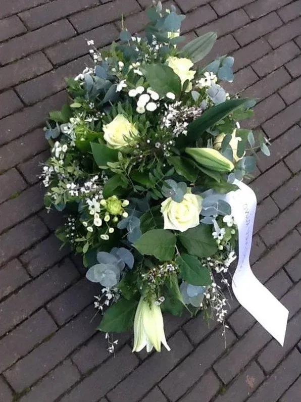 Rouwstuk van witte rozen, lelies en eucalyptus met een lint