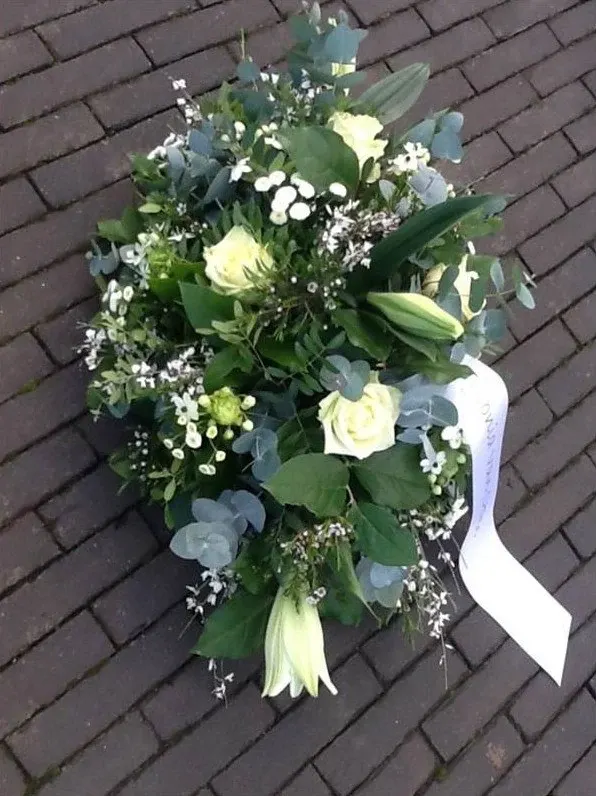 Rouwstuk van witte rozen, lelies en eucalyptus met een lint