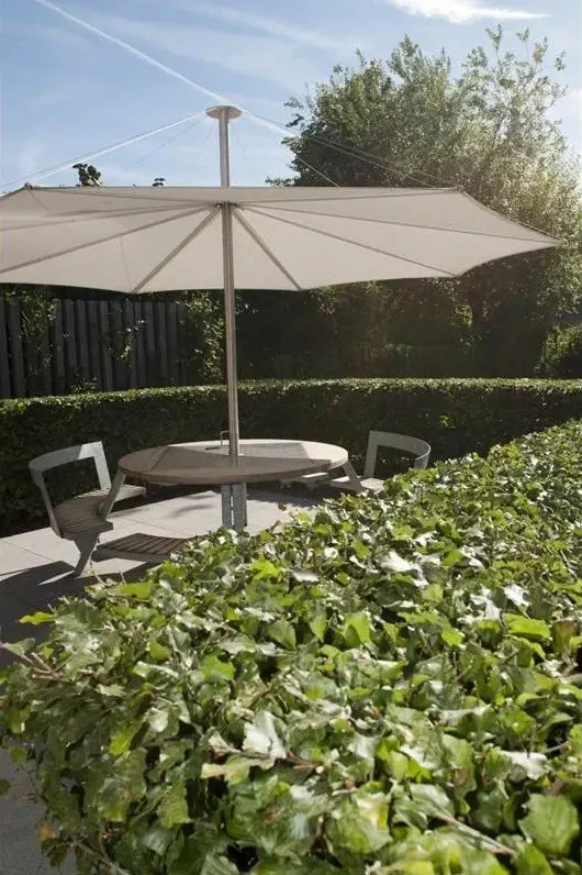 Terras met parasol en ronde tafel tussen strakke hagen