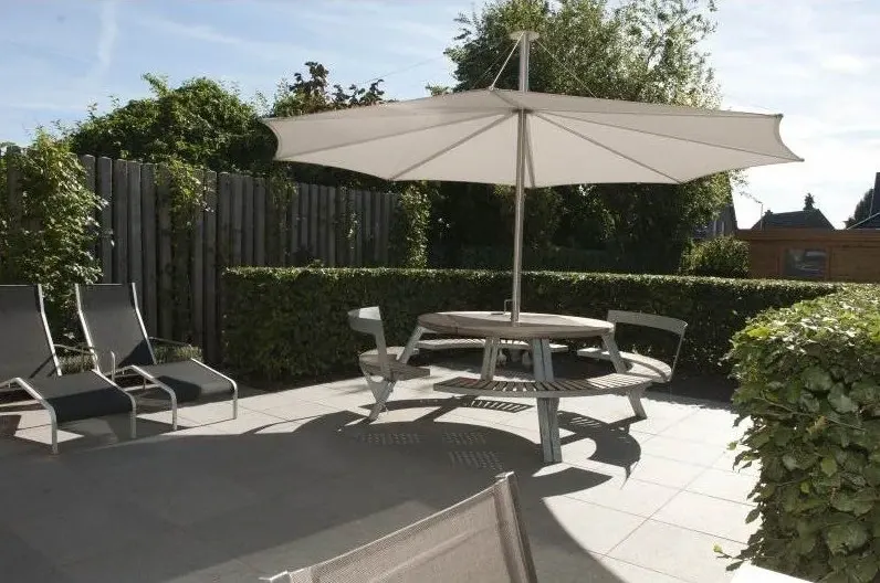 Stadstuin met een terras van grote tegels, parasol, ronde tafel en ligzetels
