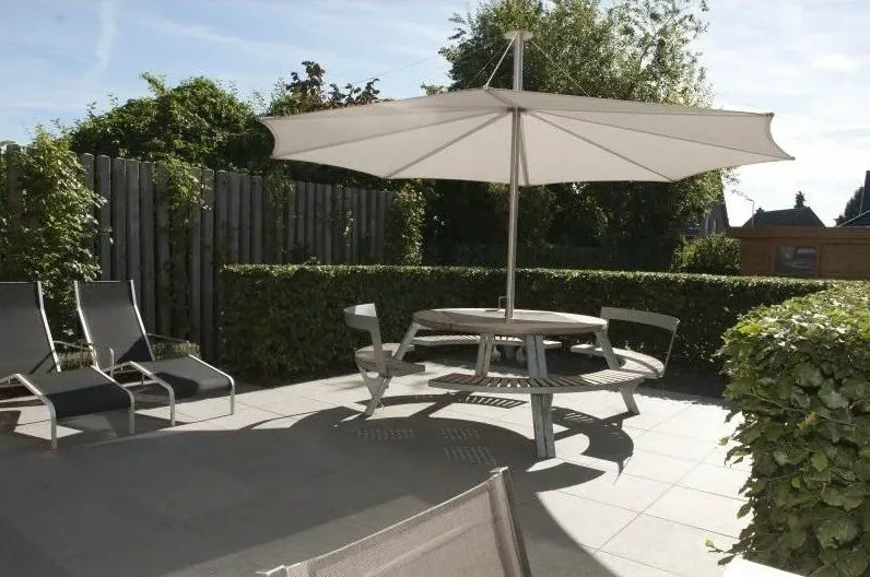 Stadstuin met een terras van grote tegels, parasol, ronde tafel en ligzetels